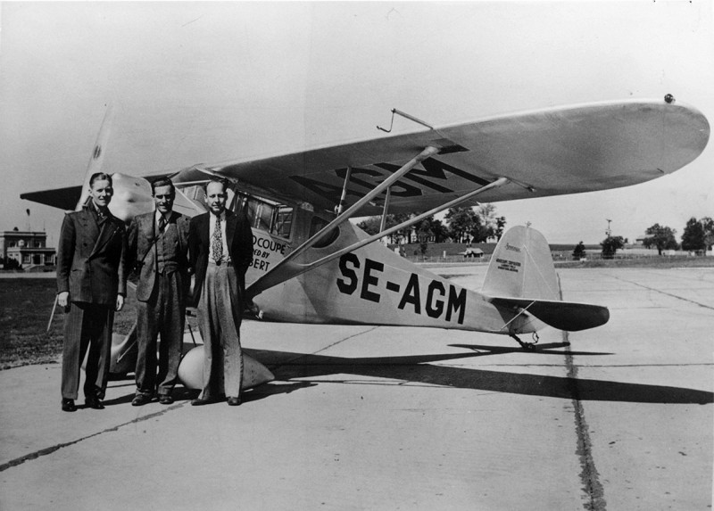 Monocoupe 90A med SE-AGM påmålad, men ej officiellt registrerad. Carl Backman står längst till vänster. Han förekommer <br />även med namnet Charlie Backman och Back Karl Andersson. Det är ej känt vilka de två andra männen är.<br />Foto ur Stig Kernells samling.