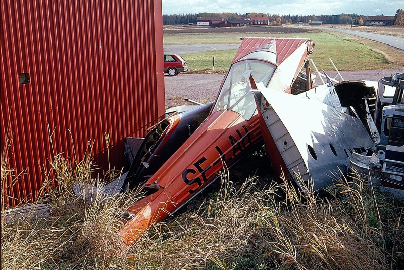 Vraket av SE-LAH efter haveri vid Bollnäs den 1991-07-29 , här invid en hangarvägg på Storvik fotograferad den 1994-10-15. <br />Foto: Hans Wallin