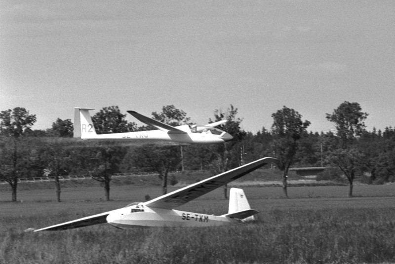 SE-TKM vid SM i segelflyg i Arboga 11-18 juni 1983. Längre bort flyger en LS1-f, SE-TRG med tävlingsmärkning R2, <br />flögs av Göran Bucht, gör här en låg överflygning i hög hastighet. Foto: Yngve Norrvi